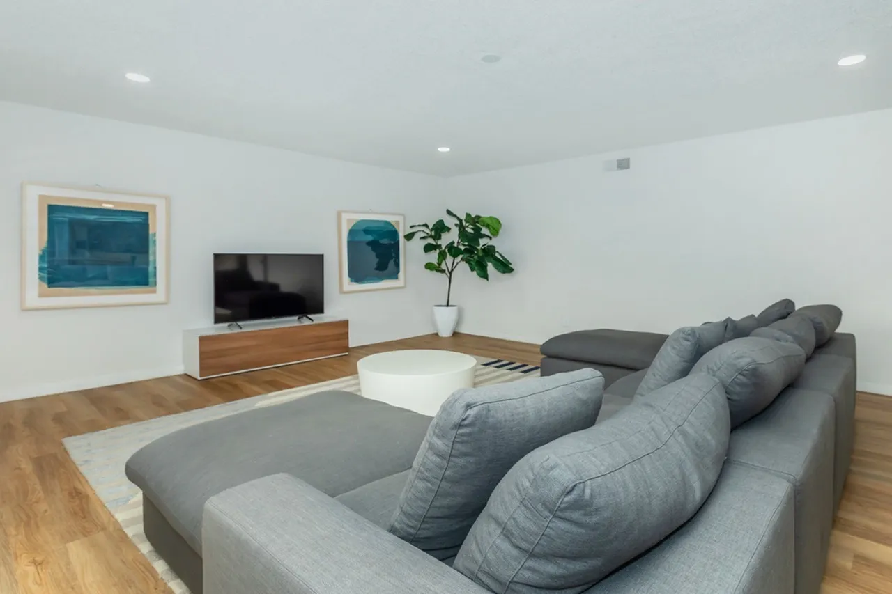 Living room, gray sectional sofa, wood-style plank flooring, wall-mounted TV, framed artwork