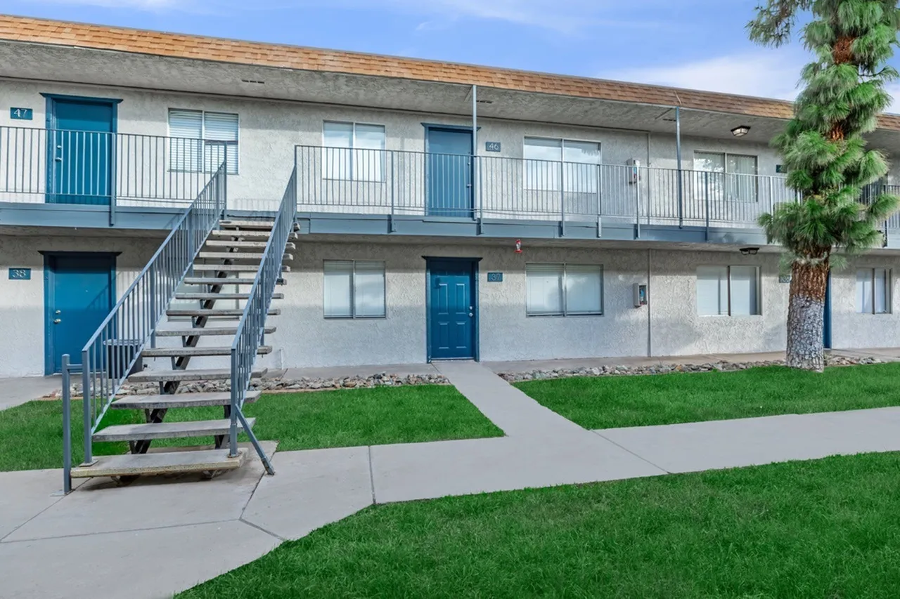Two-story apartment building, blue entry doors, metal railings, concrete walkway, manicured lawn