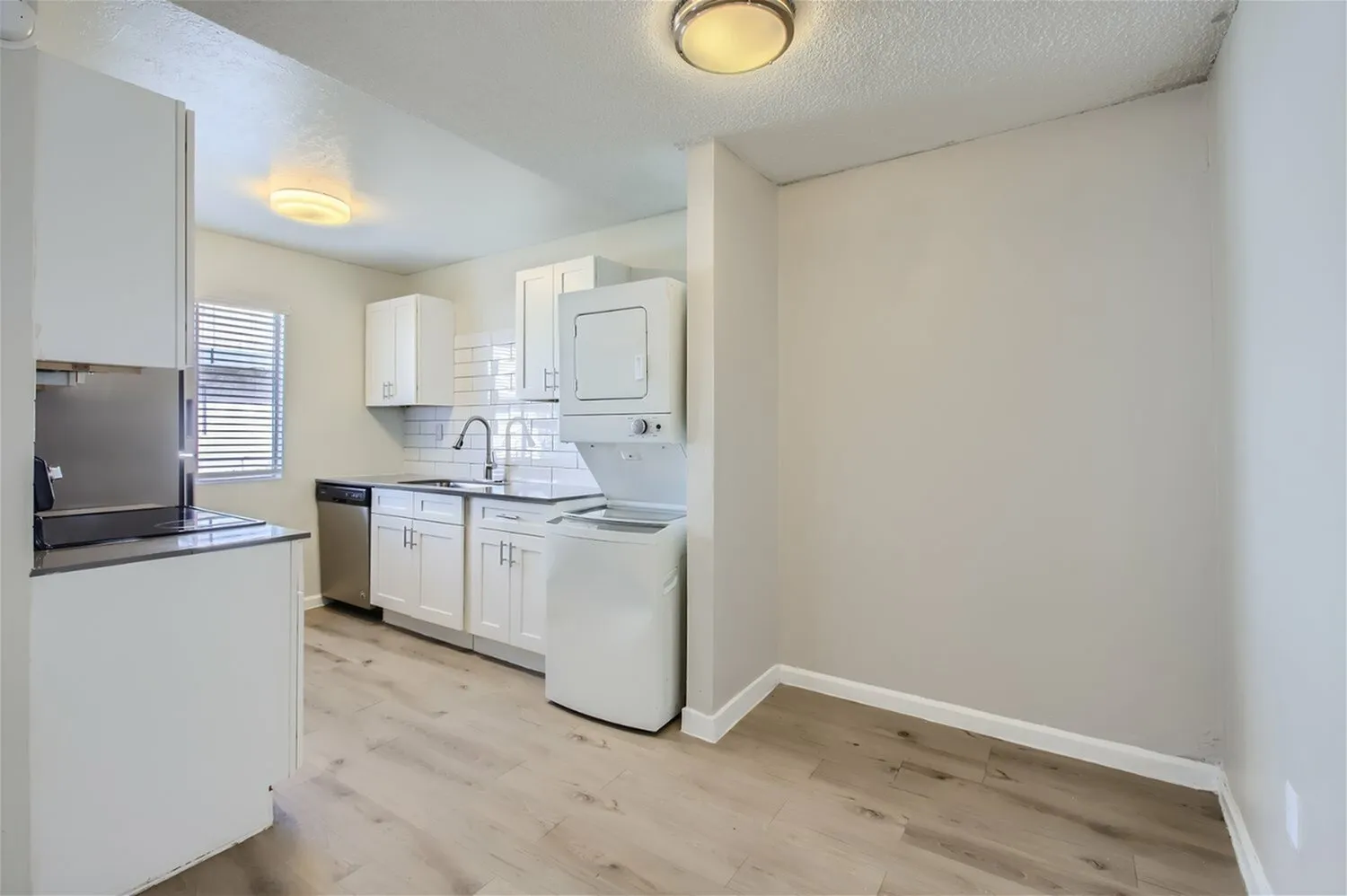 Kitchen, white shaker cabinetry, stainless appliances, black countertops, wood-style plank flooring