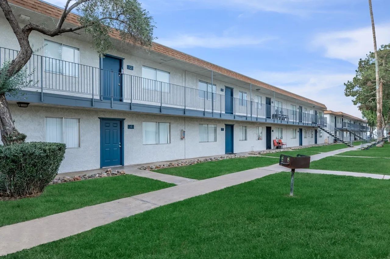 Two-story apartment building, white facade, blue doors and railings, manicured lawn, mature trees