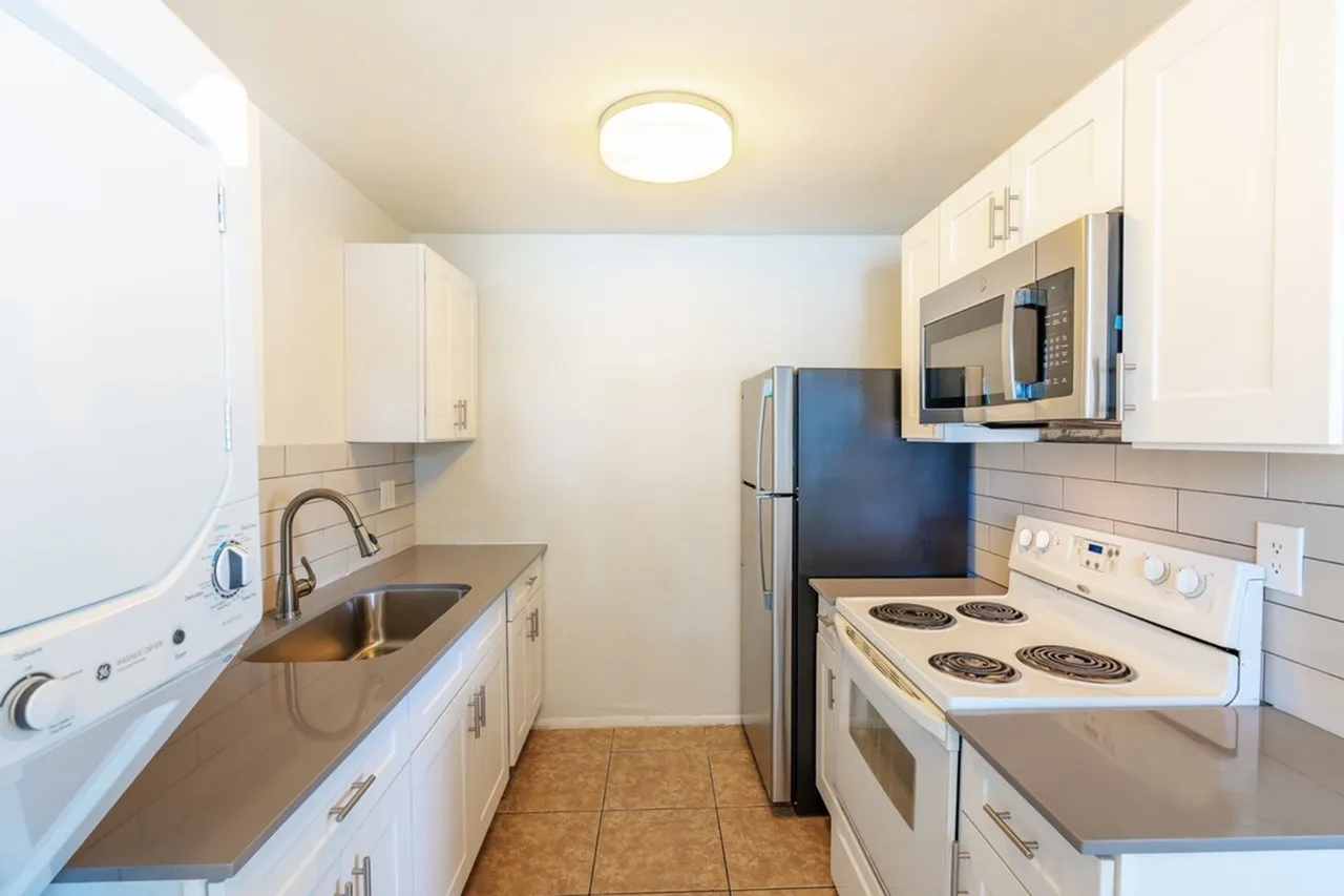 Galley kitchen, white cabinetry, stainless appliances, wood-style plank flooring