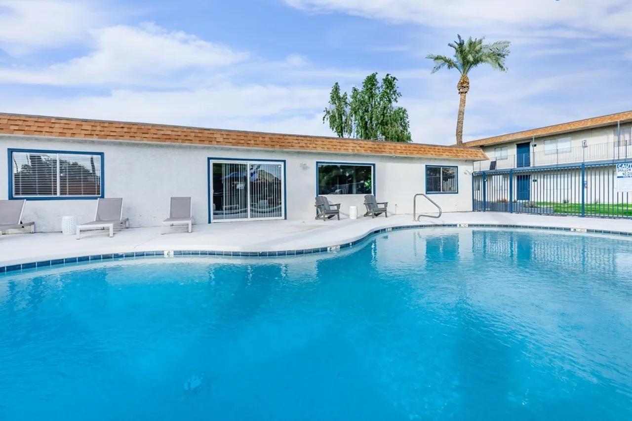 Swimming pool, white lounge chairs, poolside patio, palm trees, modern clubhouse