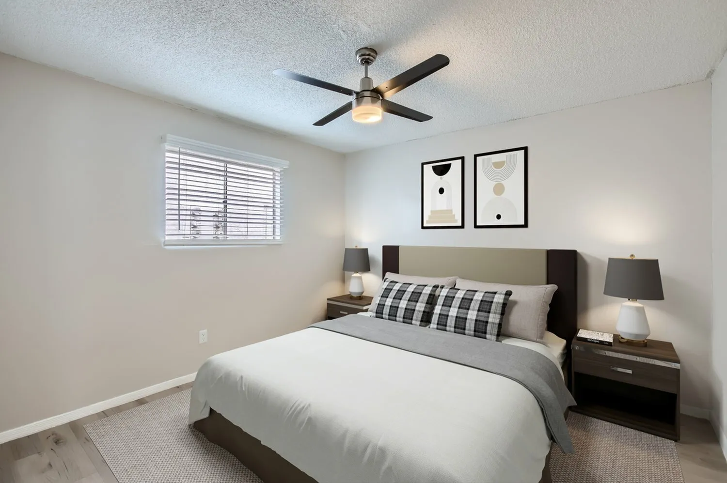 Primary bedroom, black ceiling fan with light, wood-style plank flooring, dark wood nightstands, framed wall art