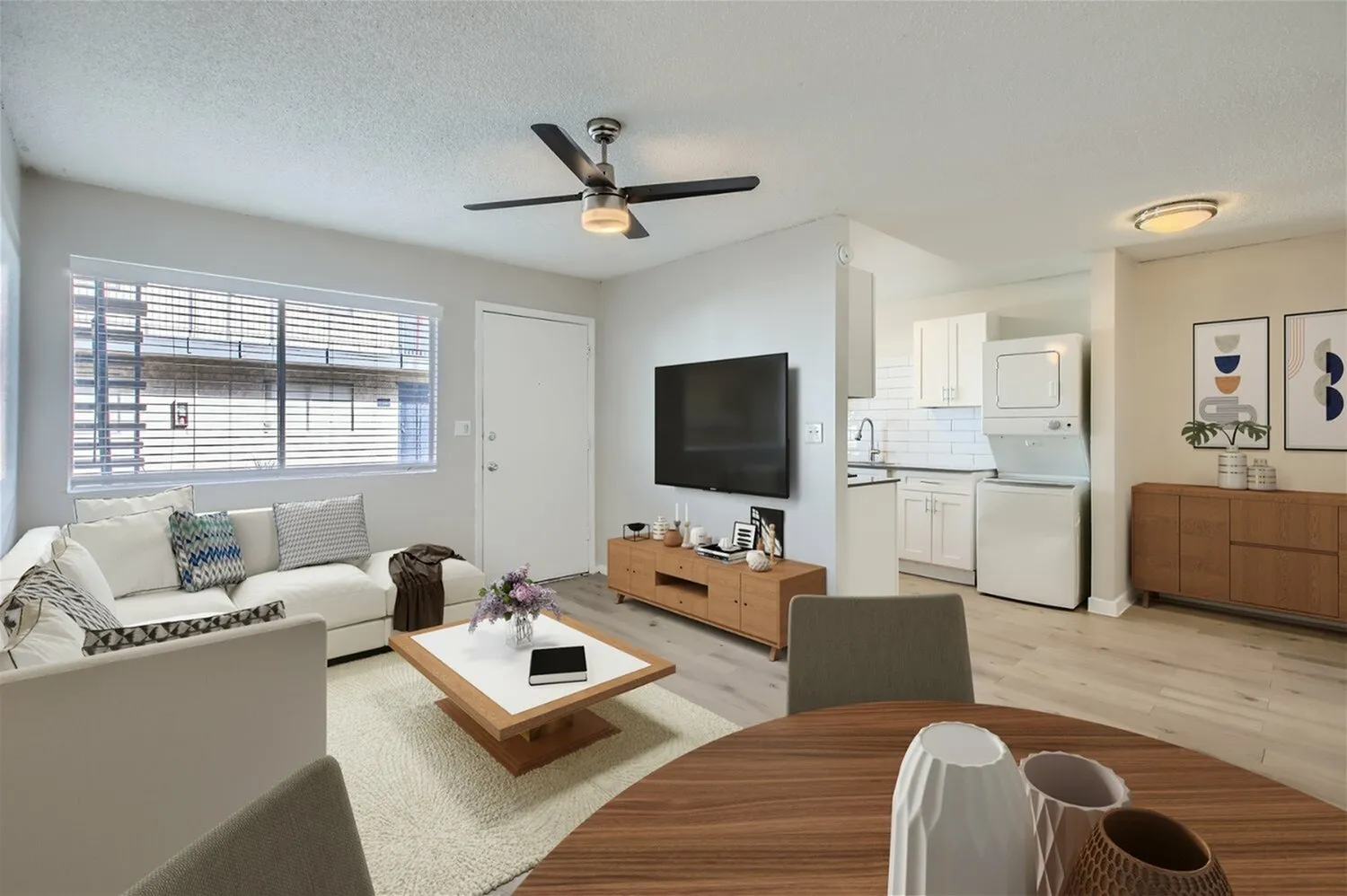 Living room with wood-style plank flooring, ceiling fan, white cabinetry, TV mounted on wall