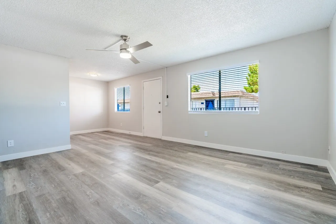 Living room with wood-style plank flooring, ceiling fan, entry door, windows with blinds