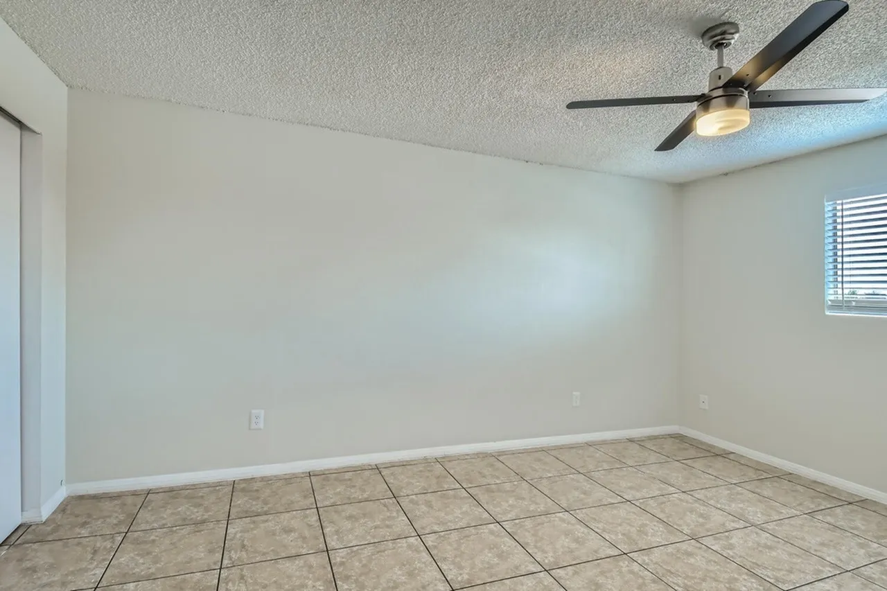 Living room, tile flooring, cream walls, ceiling fan with light fixture, window with blinds