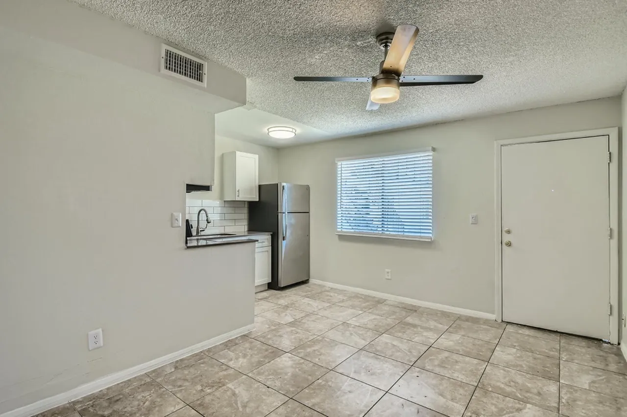 Kitchen with stainless steel appliances, white cabinetry, living area with wood-style plank flooring, ceiling fan, large window
