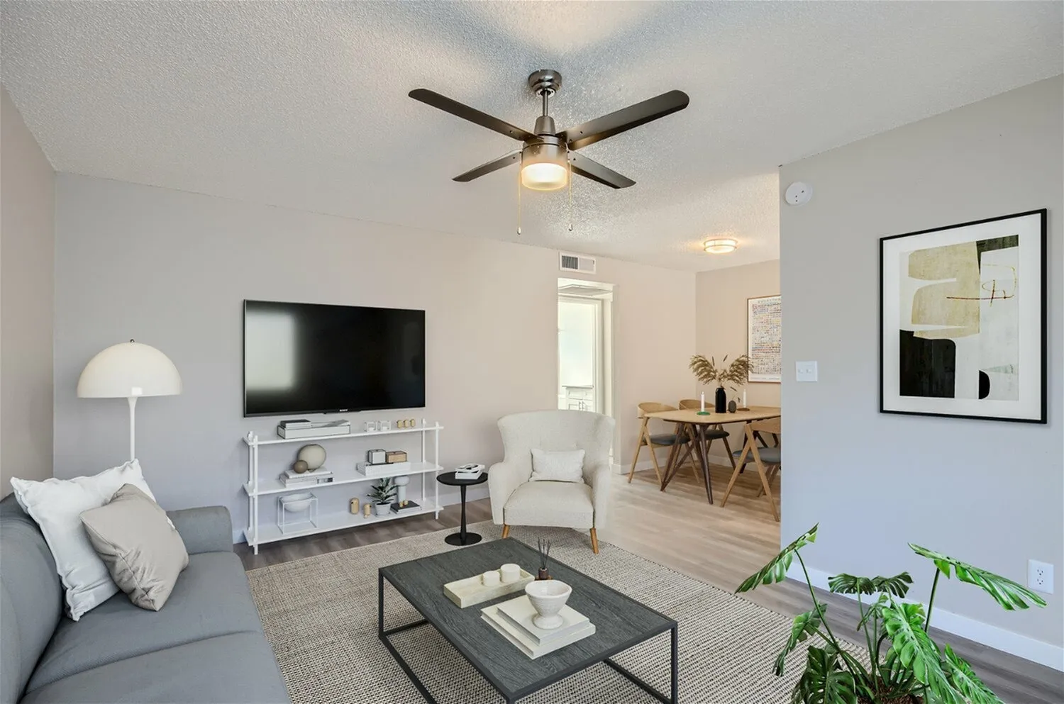 Living room with gray sofa, ceiling fan, wood dining table, white media console, wood-style plank flooring