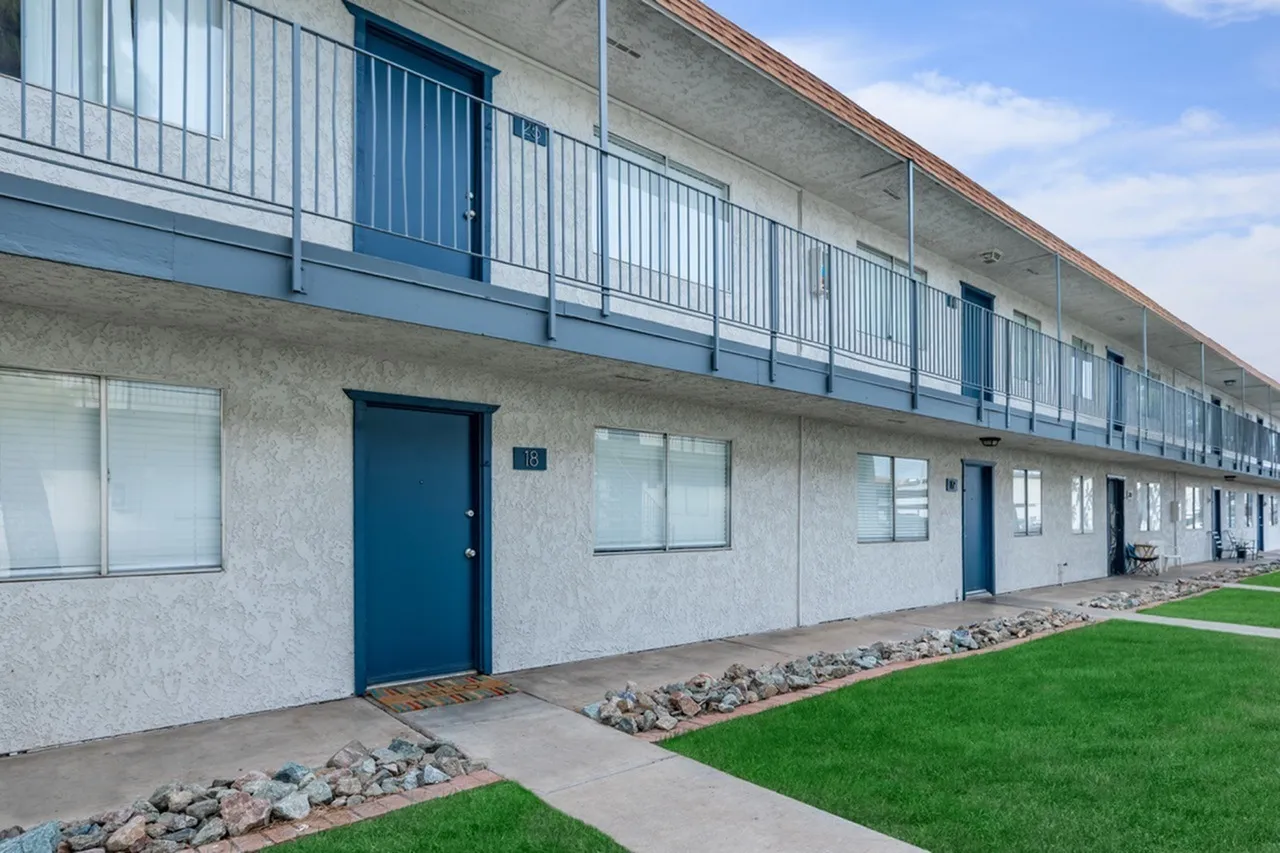 Building exterior with concrete facade, blue entry door, metal railings, green lawn