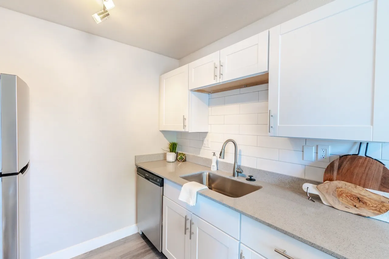 Kitchen with white shaker cabinetry, quartz countertops, subway tile backsplash, stainless appliances, wood-style plank flooring