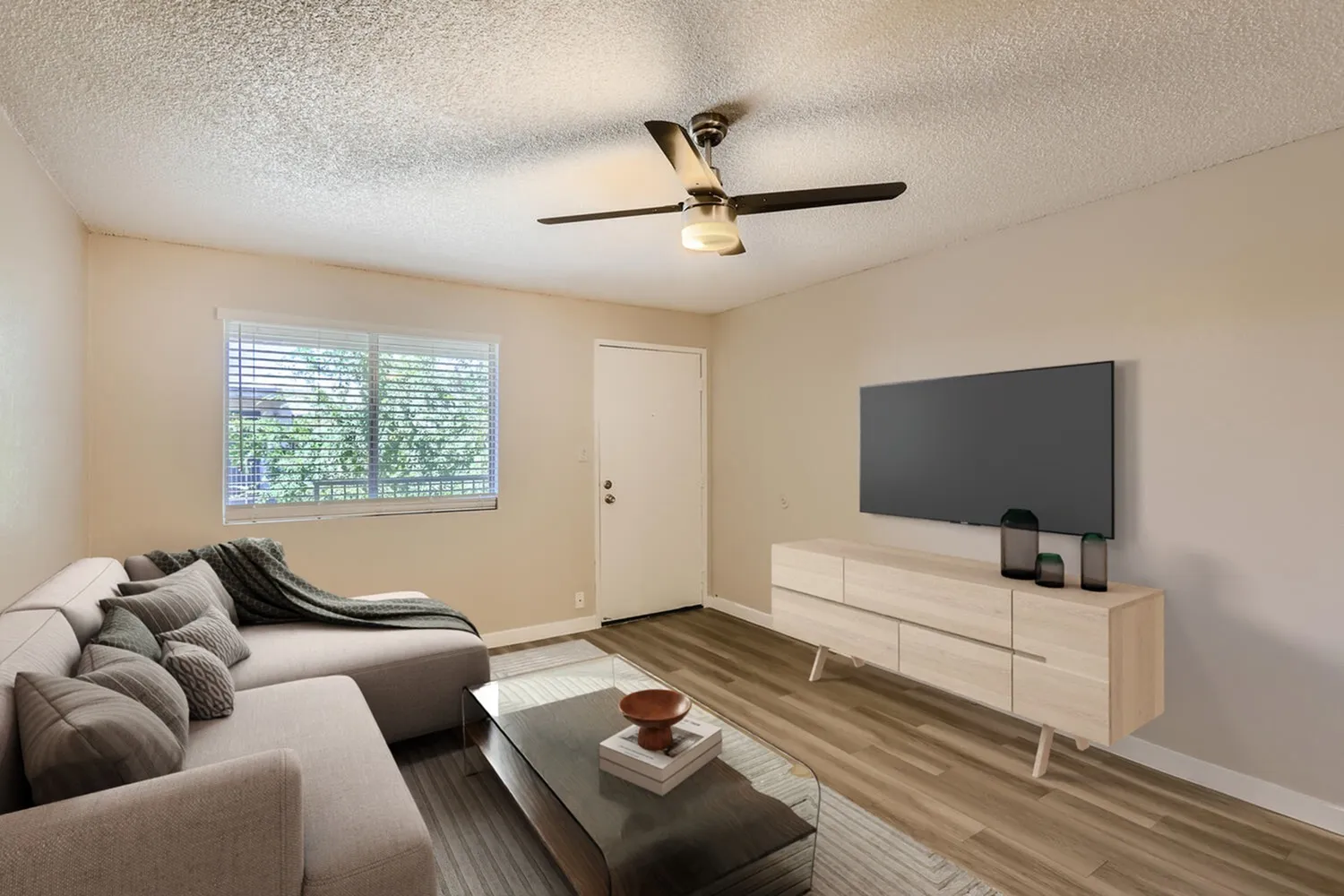 Living room with wood-style plank flooring, ceiling fan, flat-screen TV, gray sofa, windows with blinds