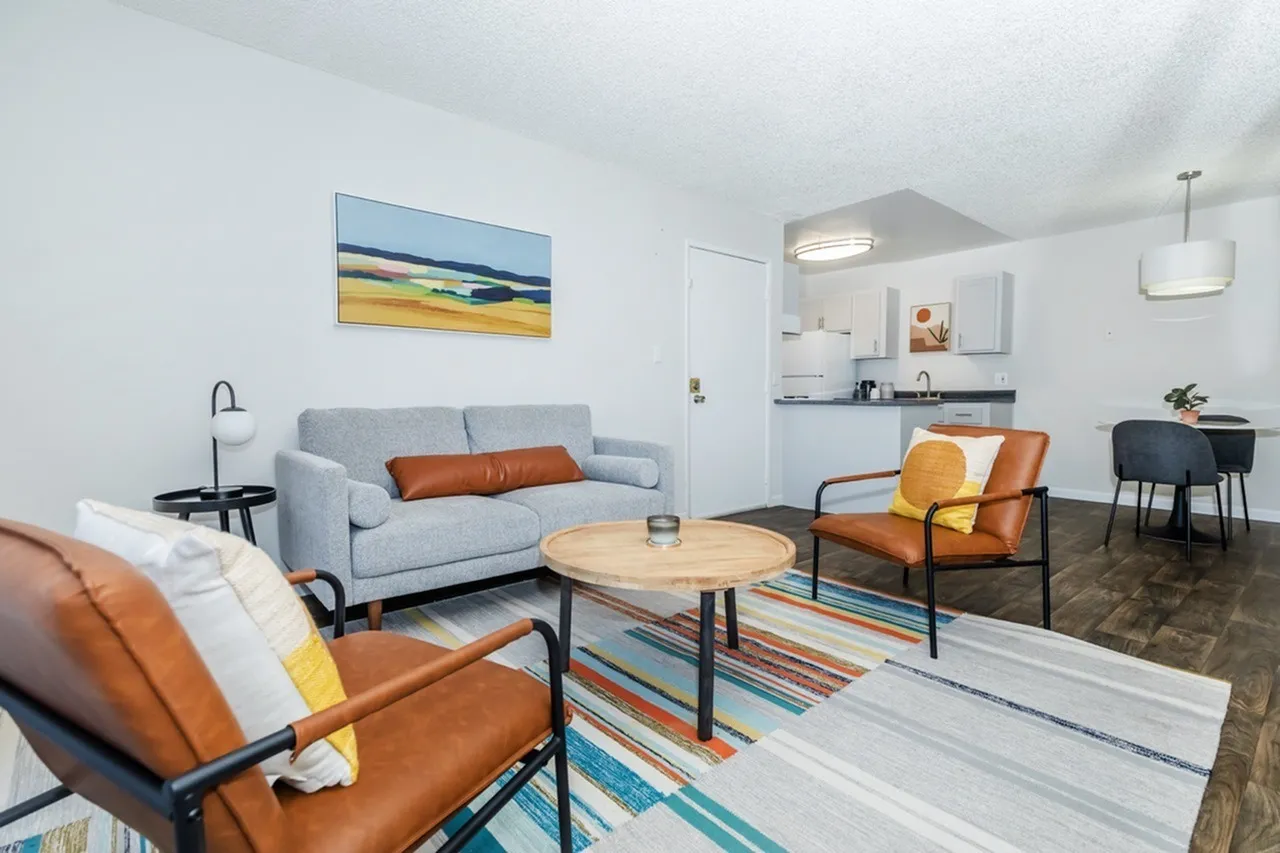 Living room with gray sofa, orange leather chairs, wood-style plank flooring, open kitchen with white cabinetry