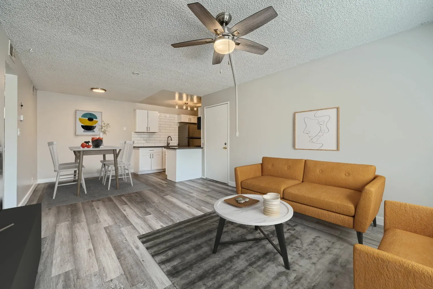 Open concept living space, wood-style plank flooring, orange upholstered sofa, ceiling fan, white cabinetry