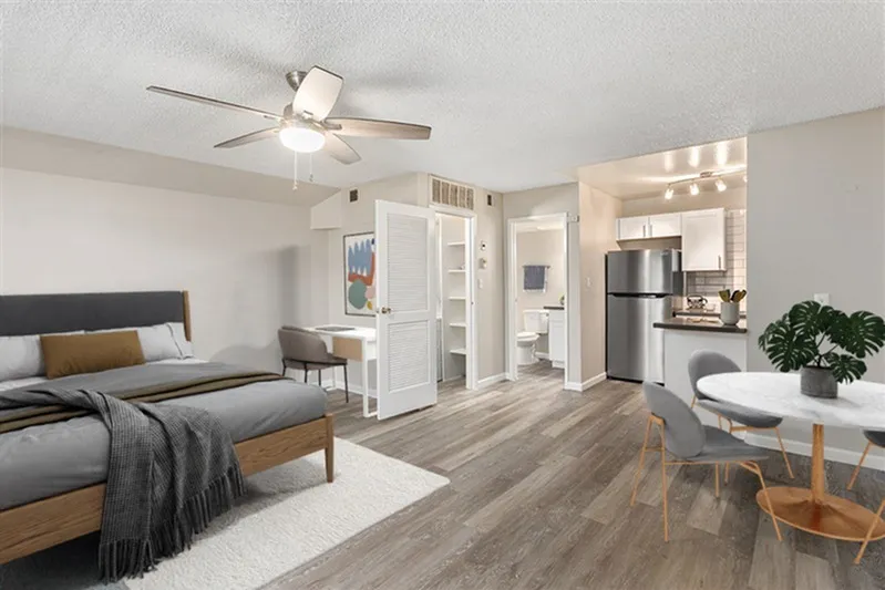 Studio interior, wood-style plank flooring, ceiling fan, stainless appliances, bathroom entrance