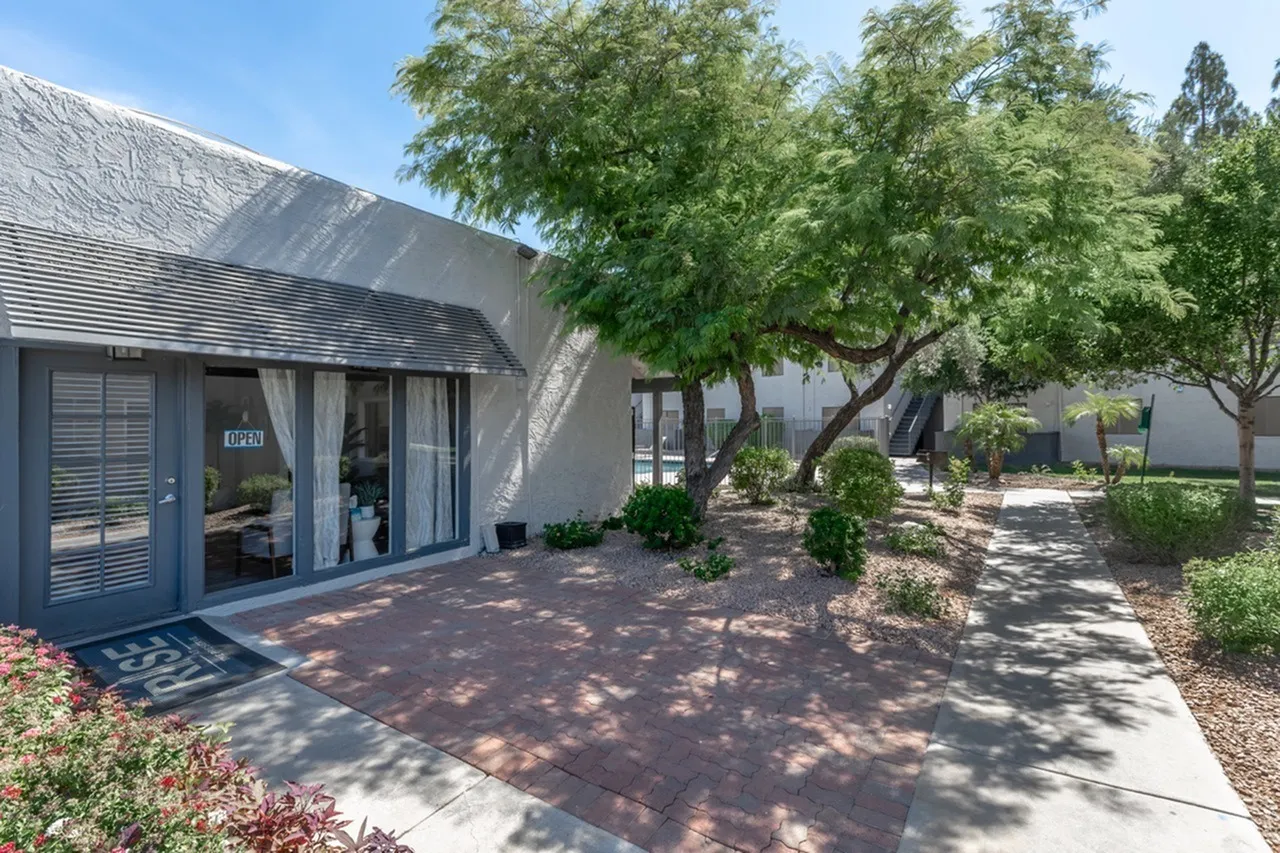 Patio area with brick pavers, slatted blue door, mature shade trees, desert landscaping