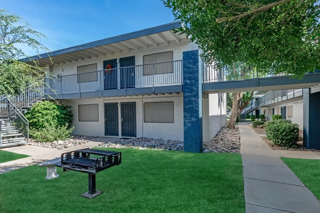 Courtyard with green lawn, picnic table, two-story residential building with white and blue exterior, metal railings, concrete pathways
