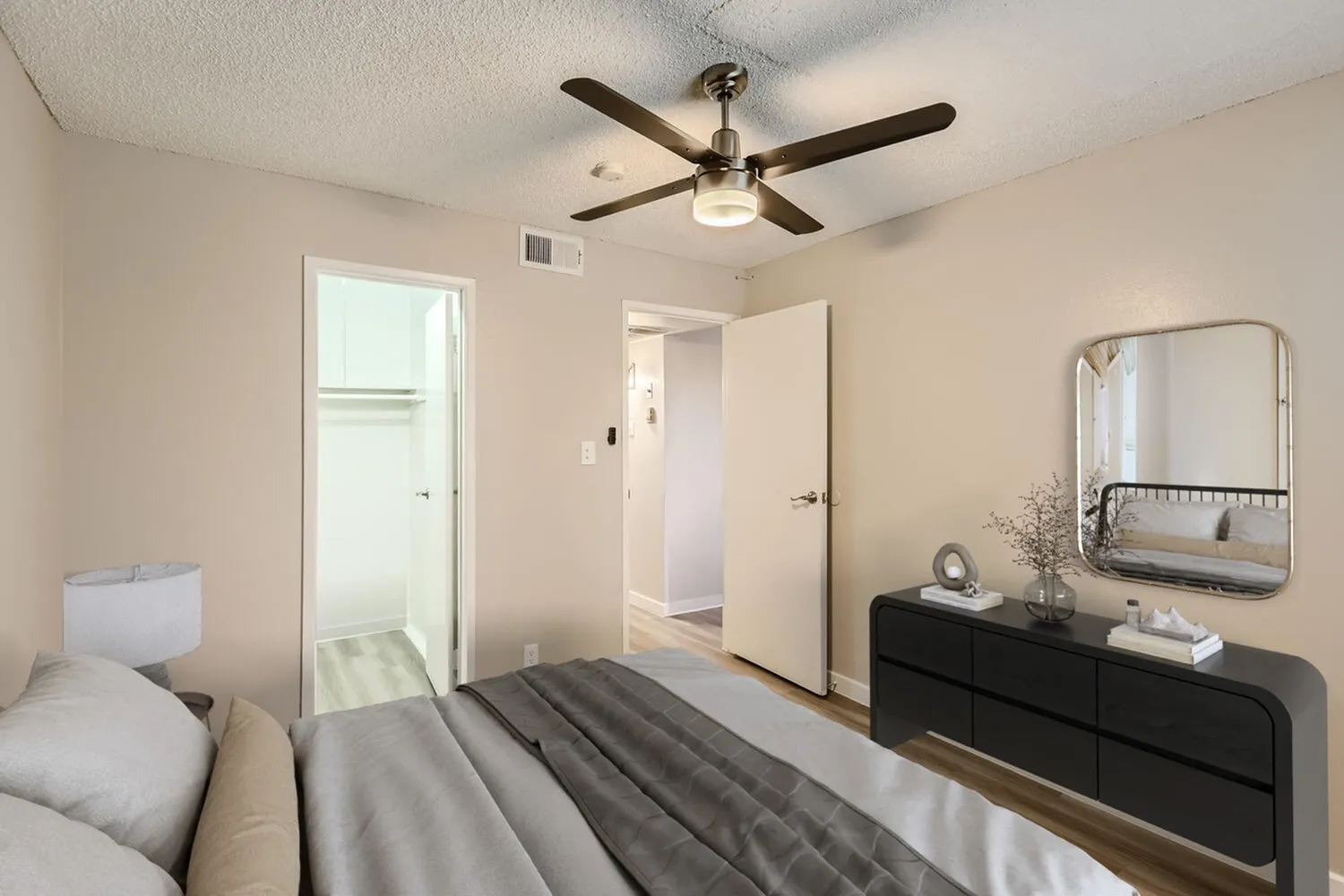 Primary bedroom, wood-style plank flooring, black ceiling fan, black dresser with mirror