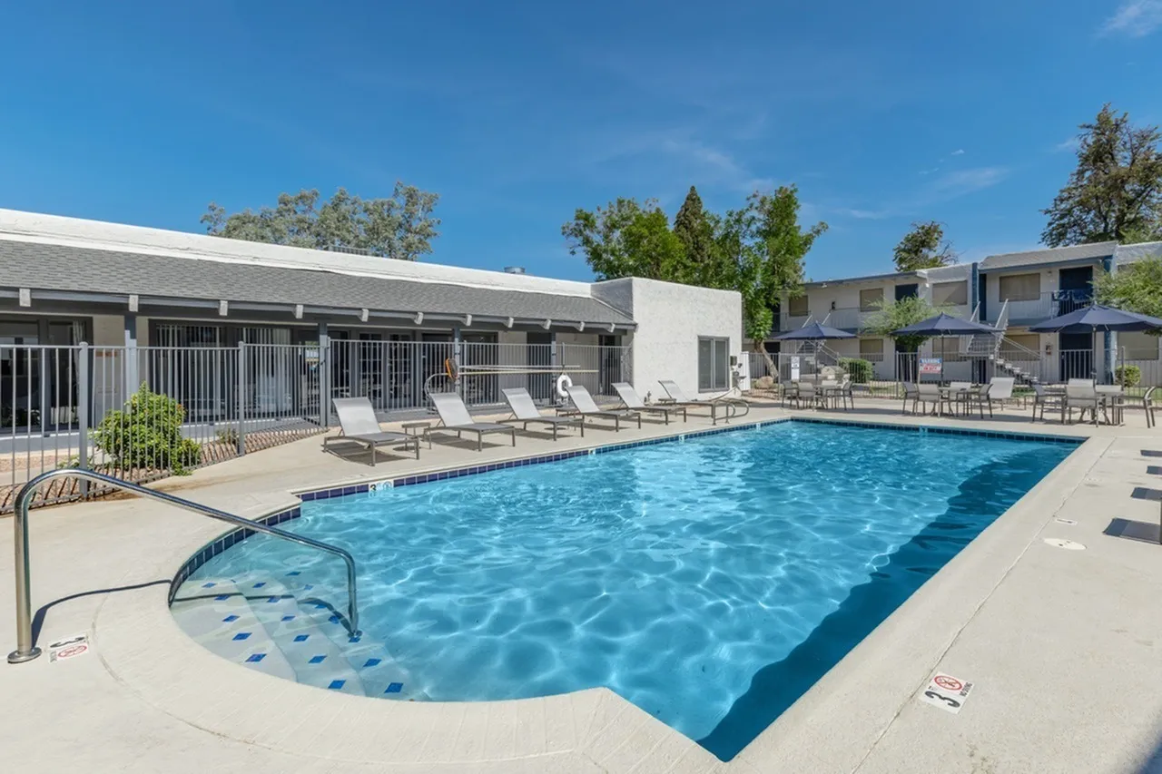 Resort-style pool, lounge chairs, metal railings, trees, clear blue water