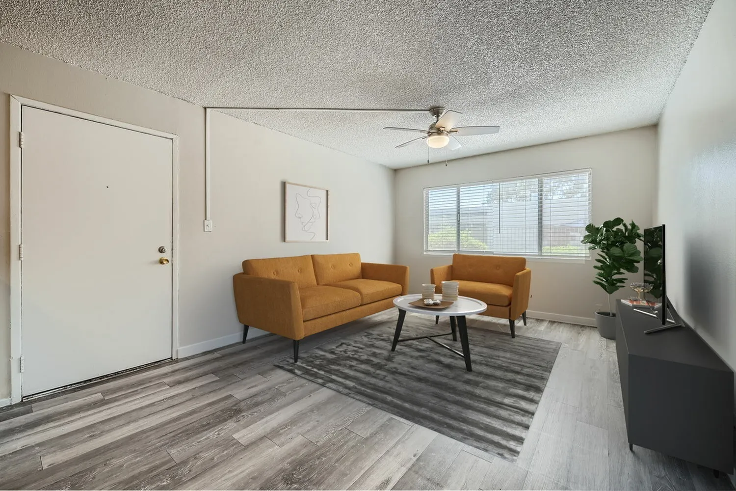 Living room, wood-style plank flooring, tan leather sofa and chair, ceiling fan, large windows