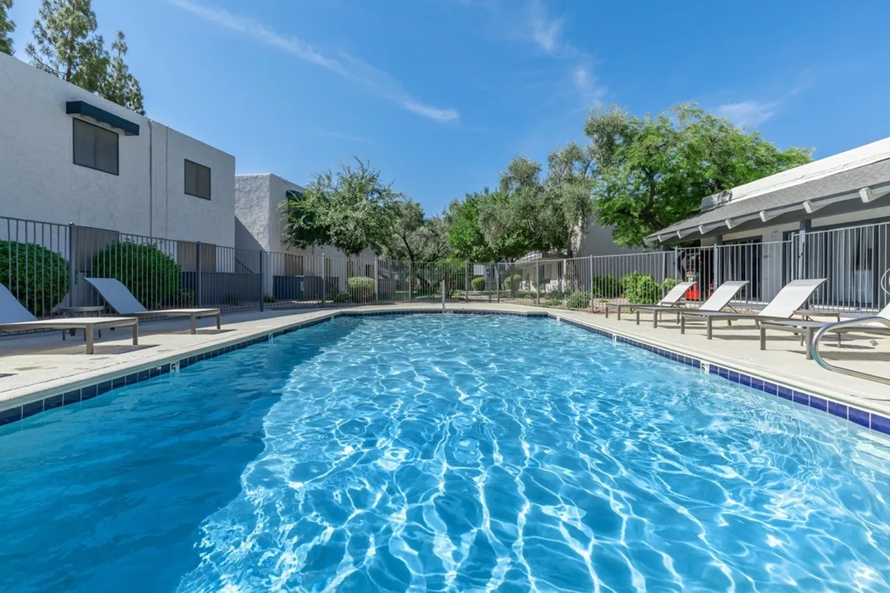 Swimming pool, lounge chairs, metal fencing, landscaping, clear blue water