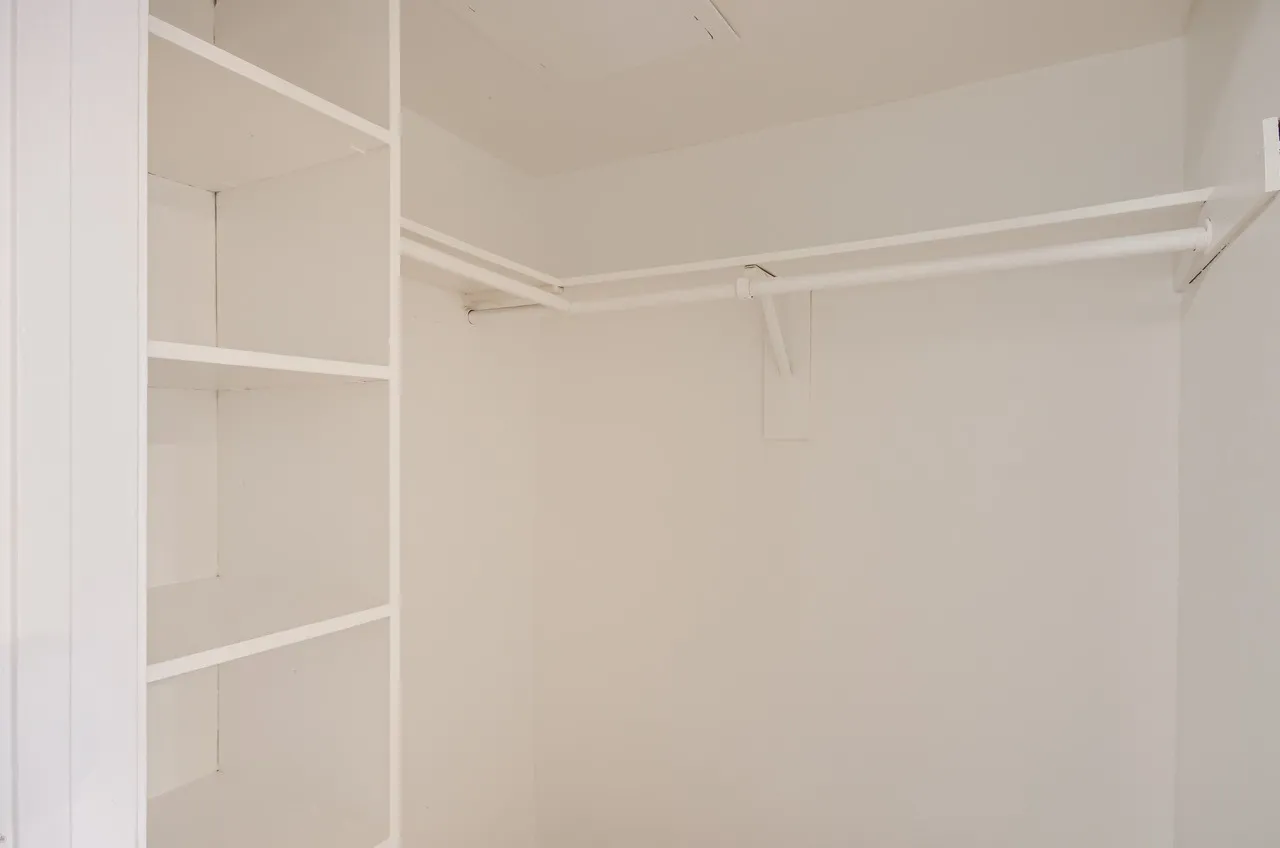 Walk-in closet, white built-in shelving, closet rod, white walls