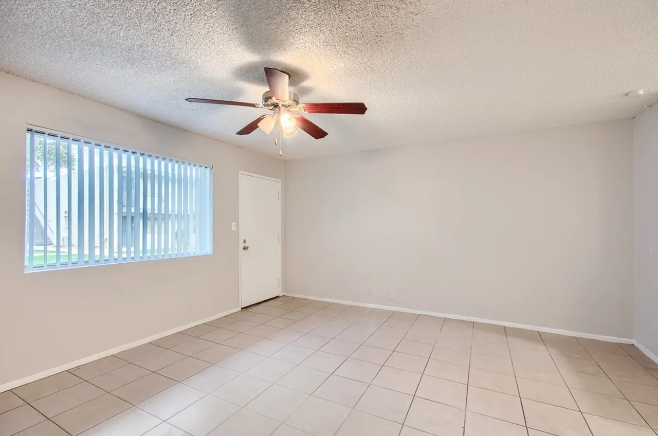 Living room with tile flooring, ceiling fan with light, vertical blinds, entry door