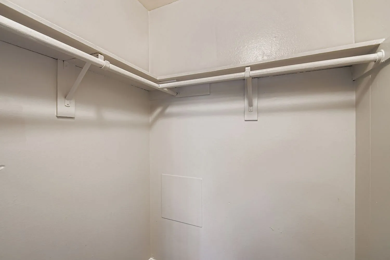 Walk-in closet, metal shelving rods, white walls, ceiling lighting