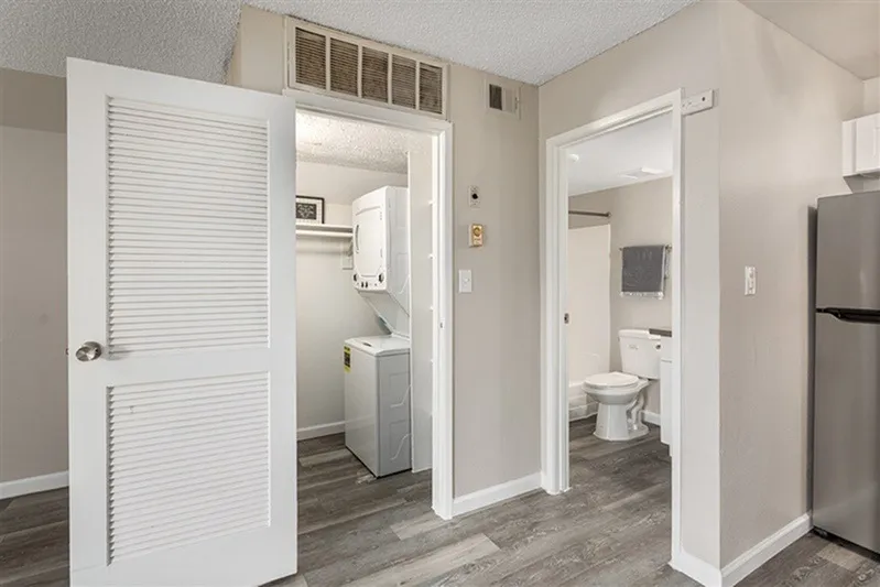 Kitchen with stainless refrigerator, laundry closet, bathroom doorway, wood-style plank flooring