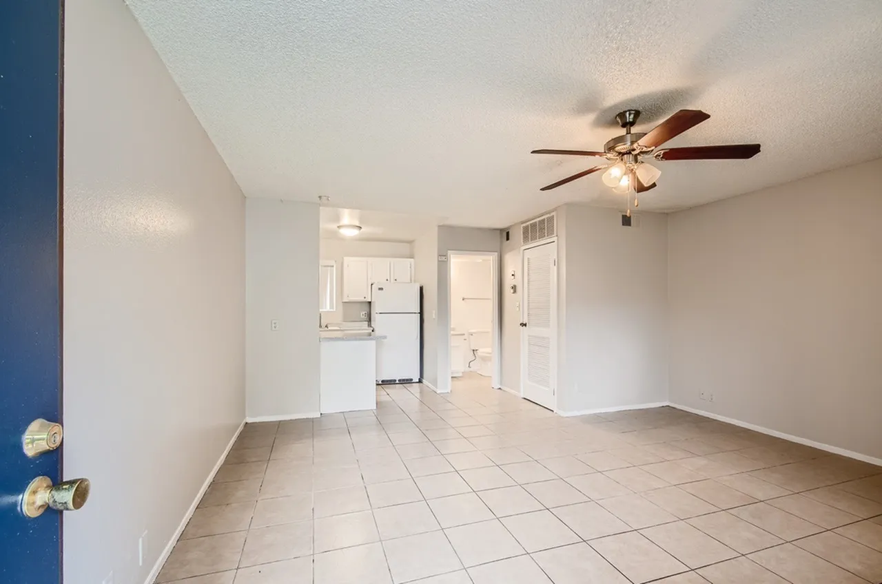Living room with wood-style plank flooring, ceiling fan, white appliances, entry door