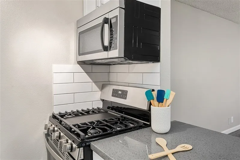 Kitchen, white subway tile backsplash, gray quartz countertops, stainless steel gas range and microwave