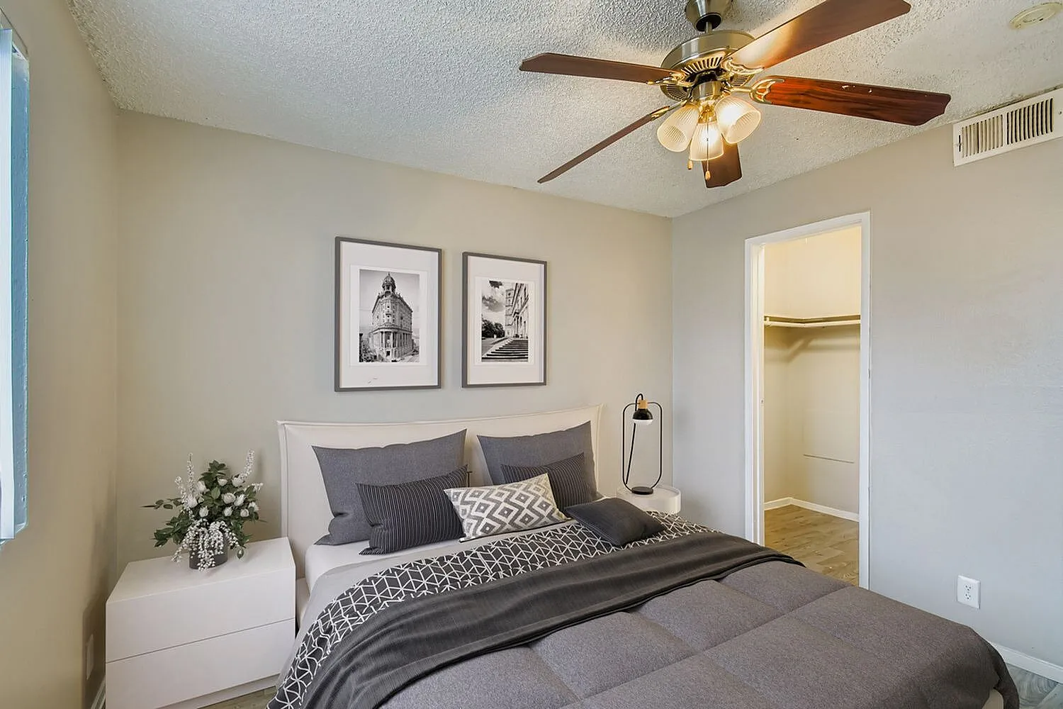 Primary bedroom, brass ceiling fan, gray bedding, white nightstand, framed wall art