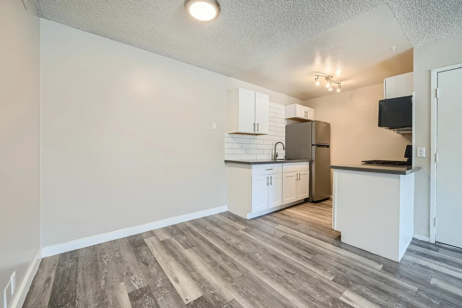 Kitchen, white shaker cabinetry, stainless steel appliances, wood-style plank flooring, breakfast bar