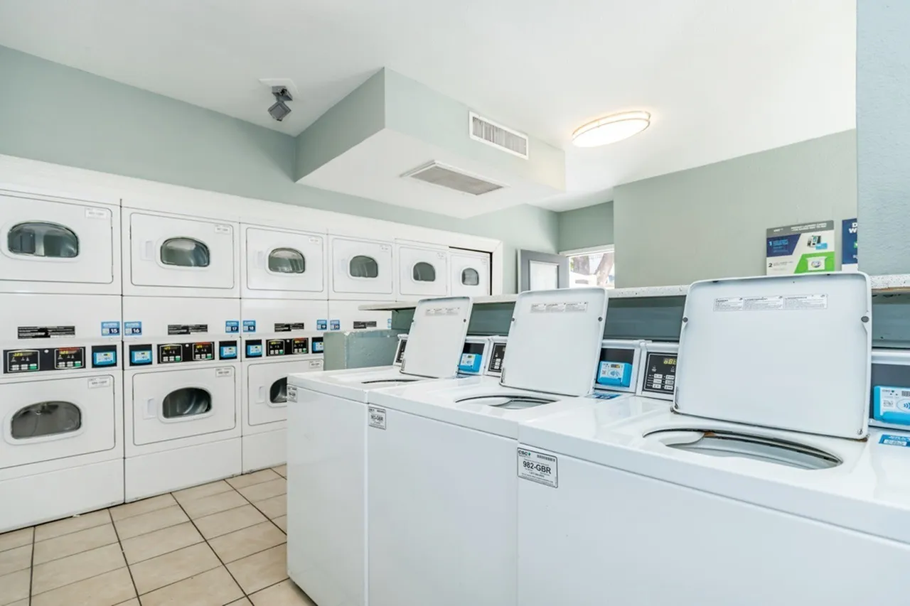Laundry room with white washers and dryers, light green walls, tile flooring, ventilation units