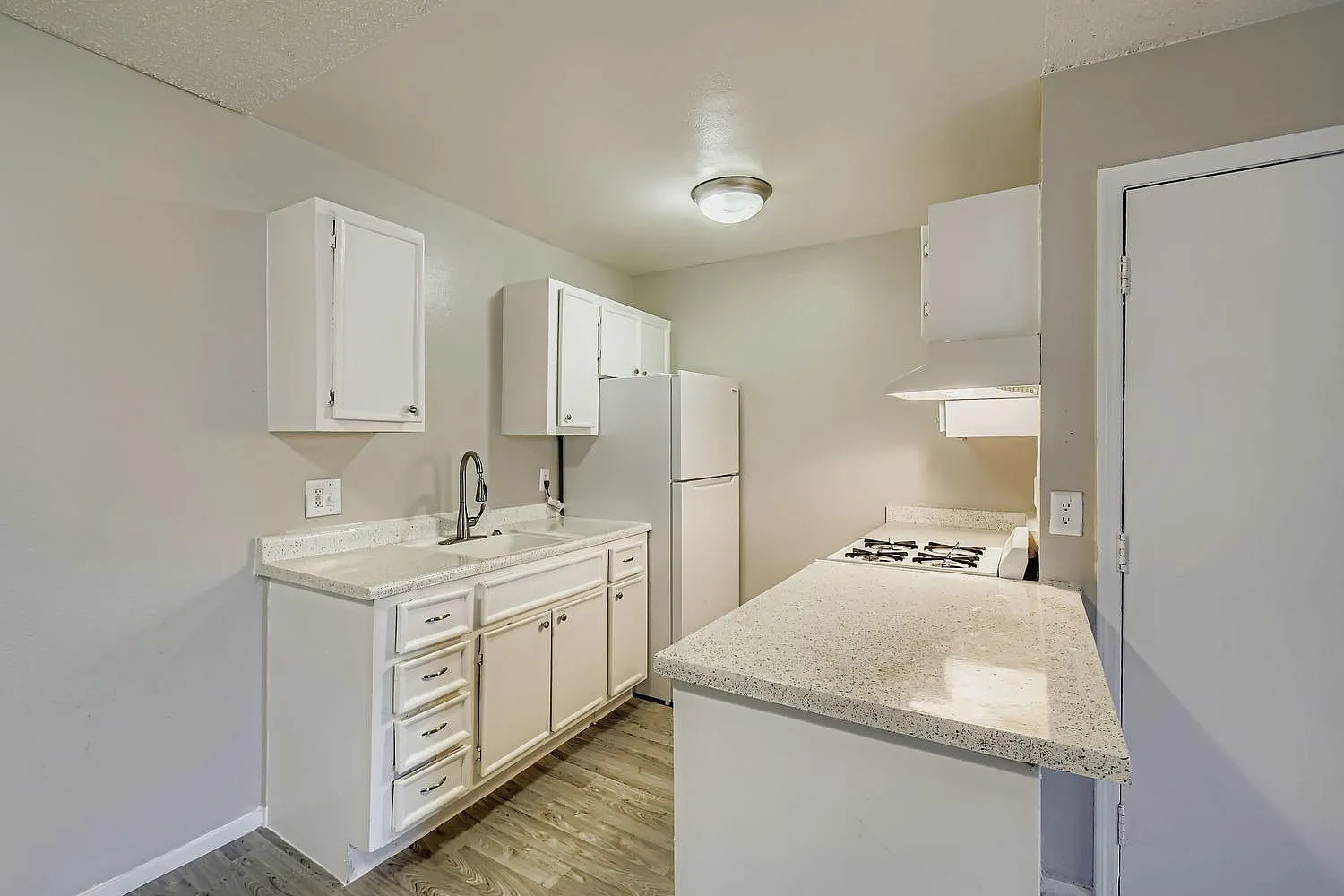 Kitchen with white shaker cabinetry, quartz countertops, stainless appliances, wood-style plank flooring