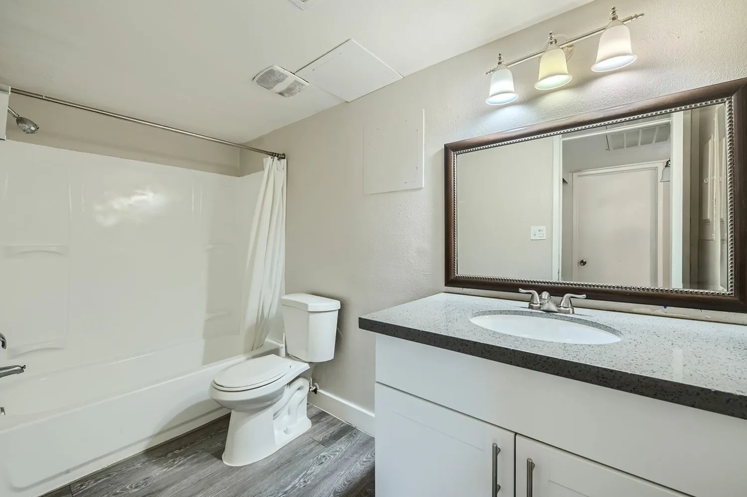 Primary bathroom, white vanity with quartz countertop, framed mirror, wood-style plank flooring