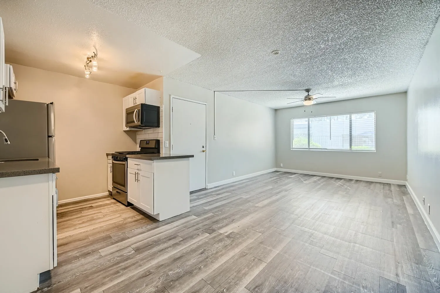 Kitchen with white cabinetry, stainless appliances, wood-style plank flooring, open to living room with windows