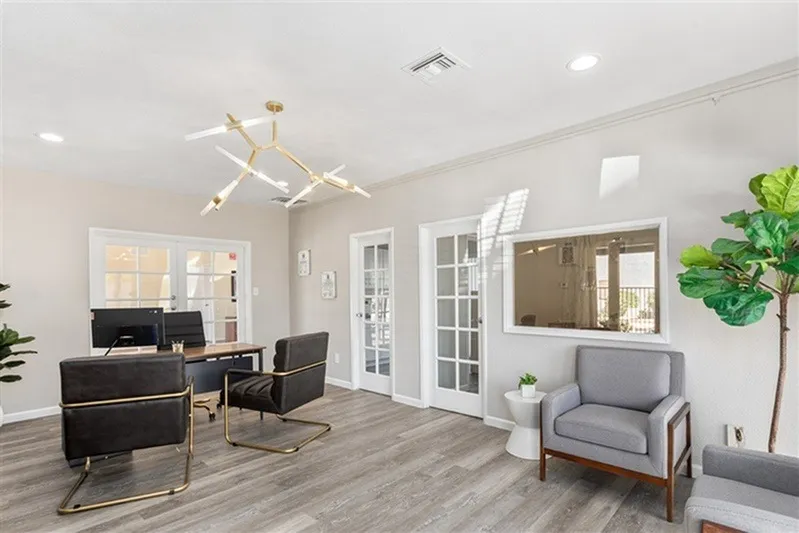 Office space, wood-style plank flooring, black desk, gray armchair, brass chandelier