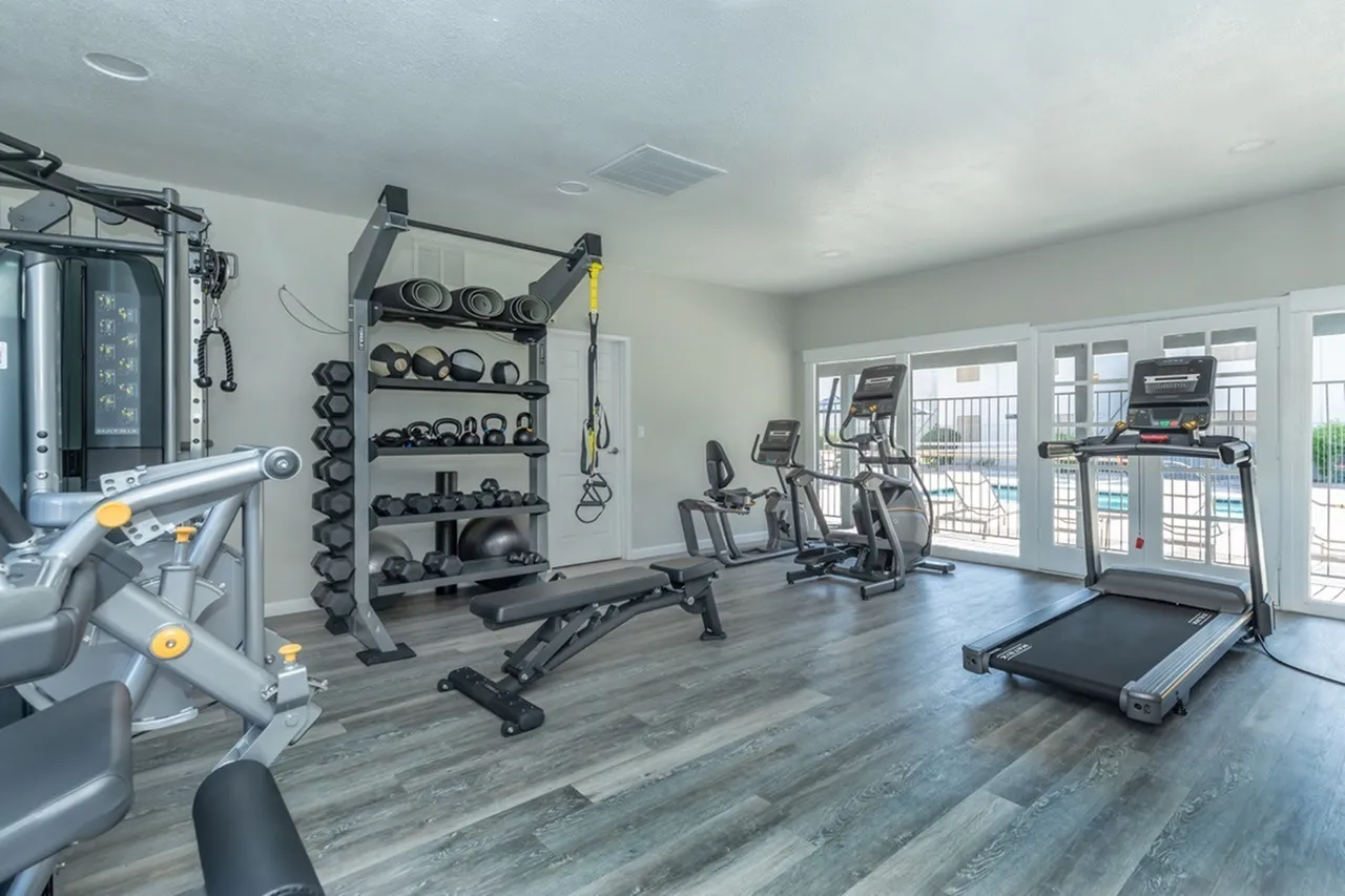 Fitness center with wood-style plank flooring, dumbbell rack, exercise machines, treadmill