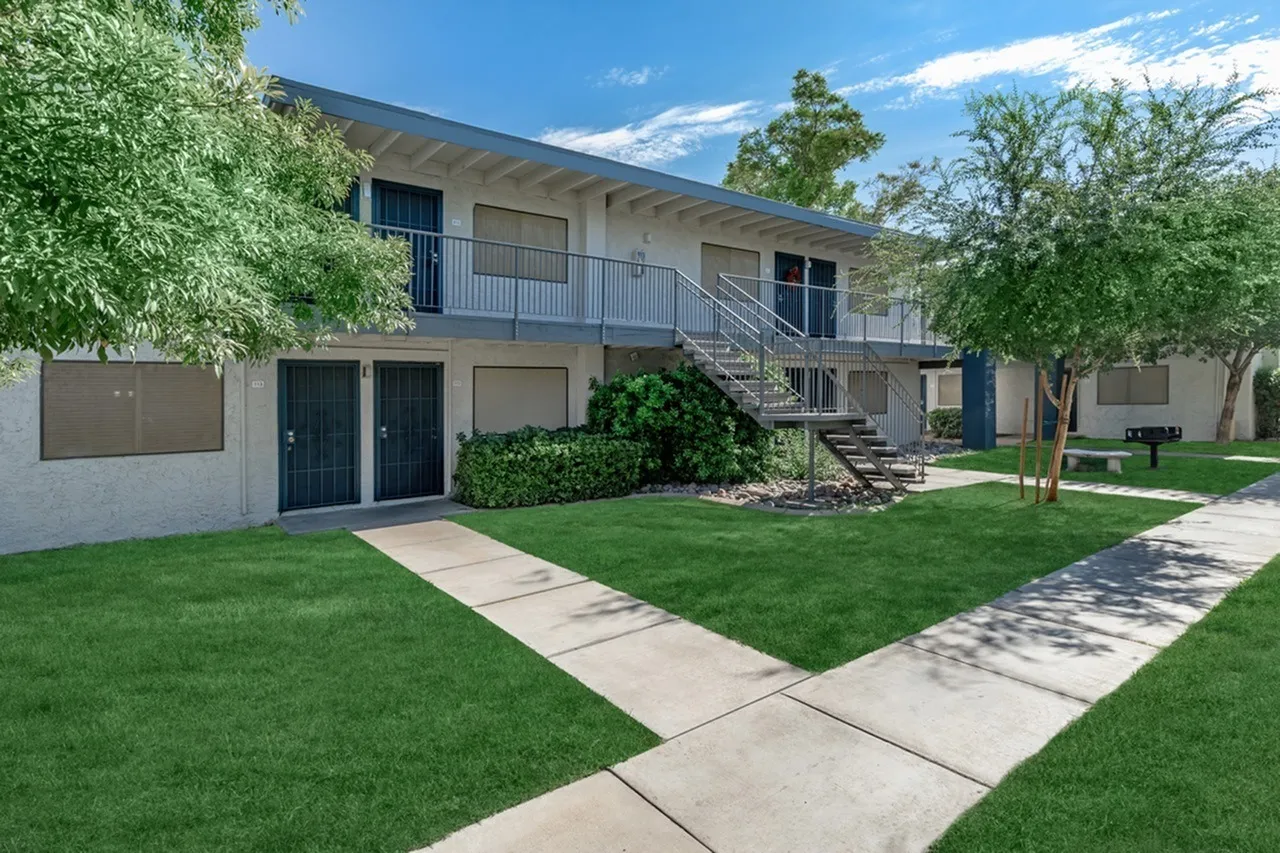 Courtyard with manicured lawn, concrete walkways, mature trees, two-story residential building with balconies and stairs, Phoenix AZ