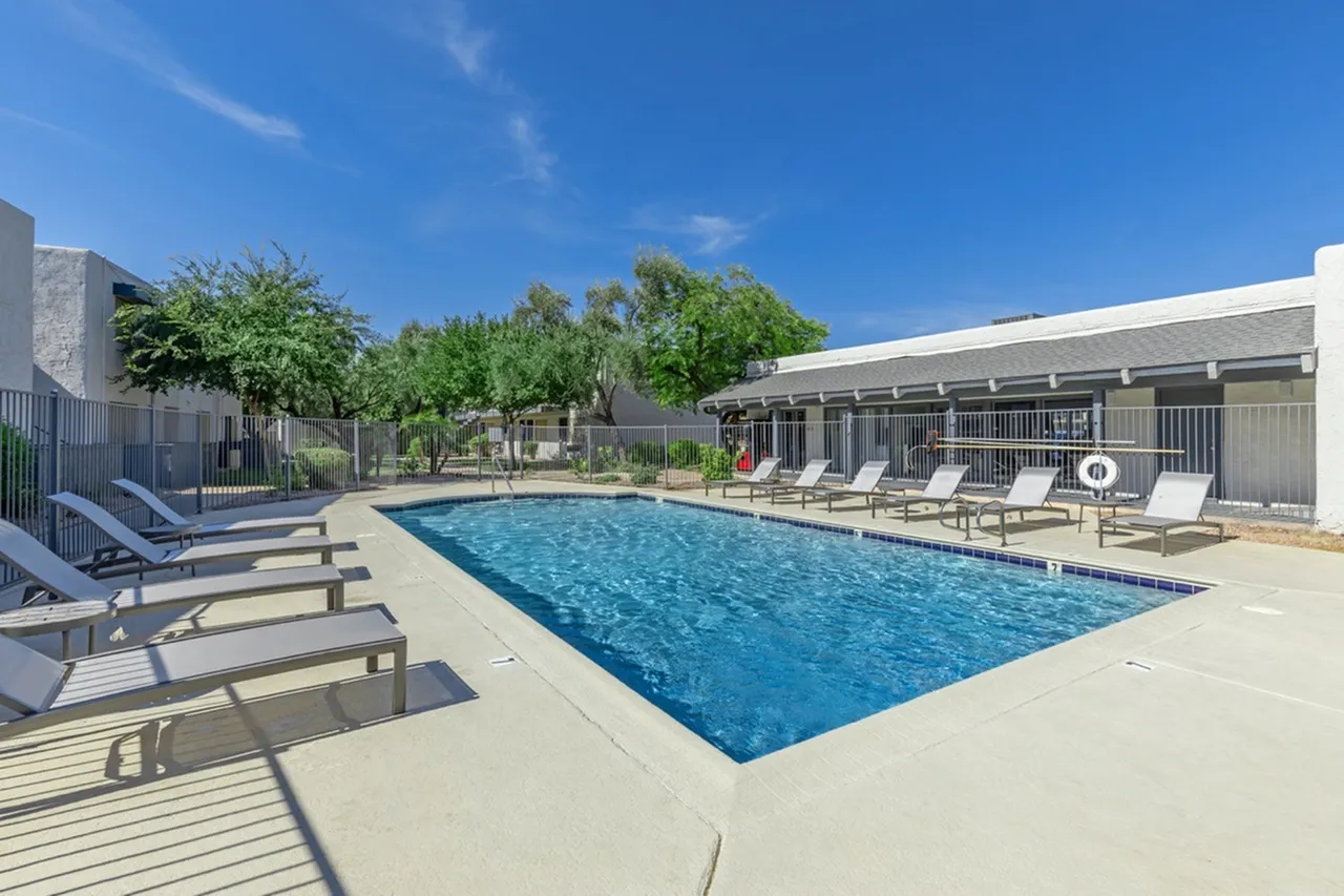 Swimming pool, lounge chairs, mature trees, covered structures, clear sky