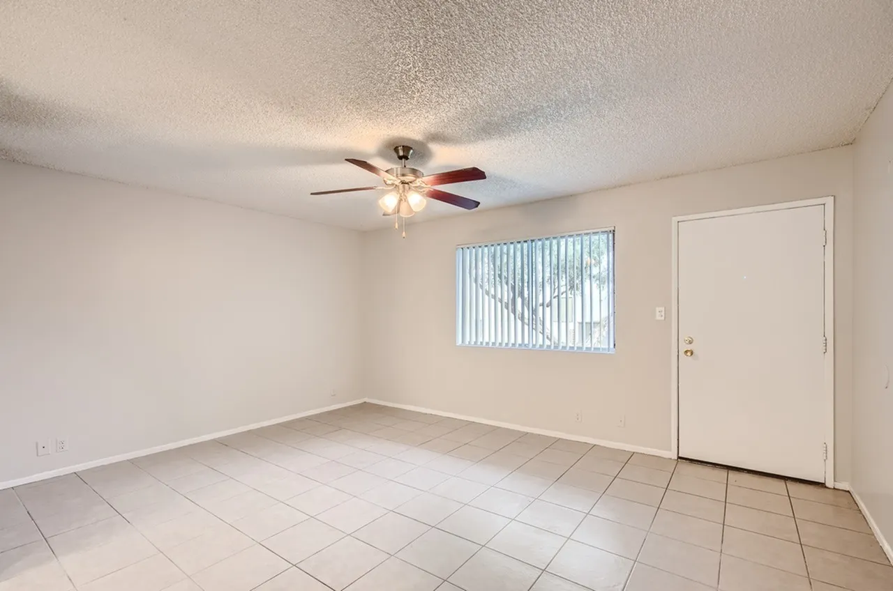Living room, ceramic tile flooring, ceiling fan with light fixture, vertical blinds, entry door