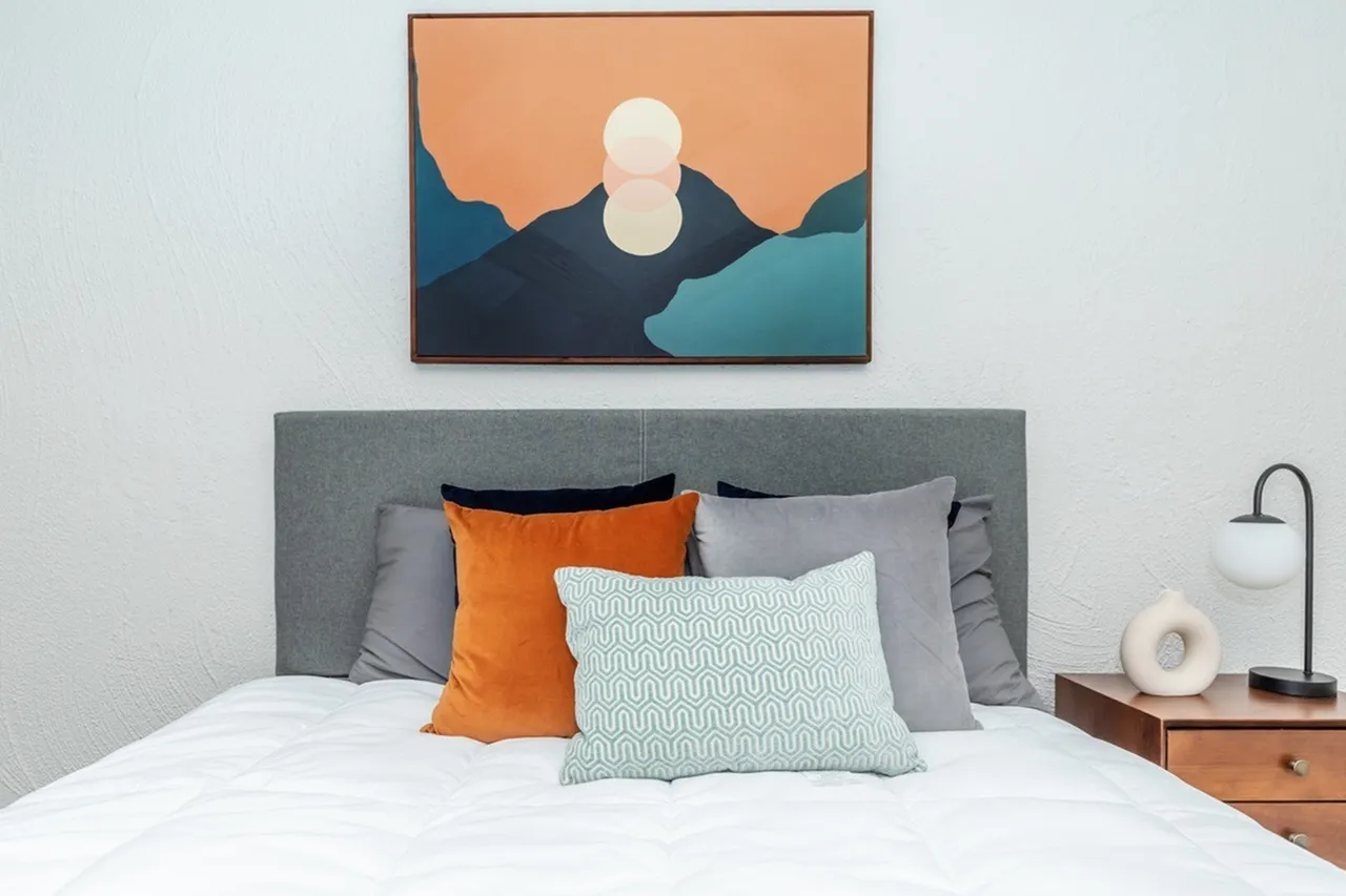 Bedroom, gray upholstered headboard, colorful throw pillows, framed landscape art