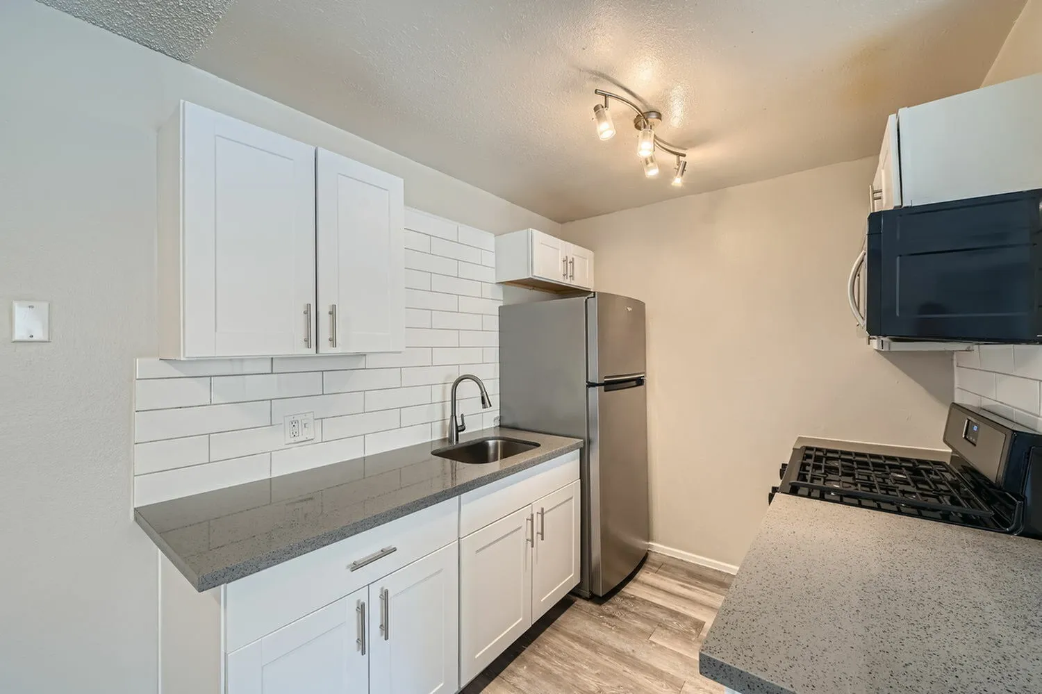Kitchen, white shaker cabinetry, gray granite countertops, stainless steel appliances, subway tile backsplash, wood-style plank flooring