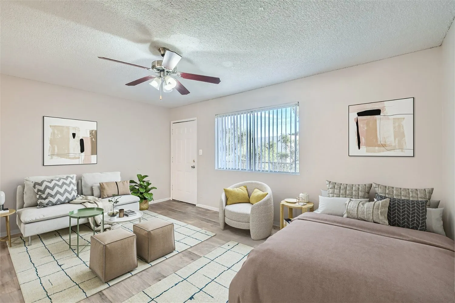 Studio apartment, wood-style plank flooring, ceiling fan, bed with gray bedding