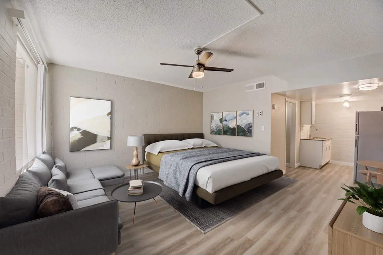 Studio bedroom, wood-style plank flooring, ceiling fan, gray upholstered seating