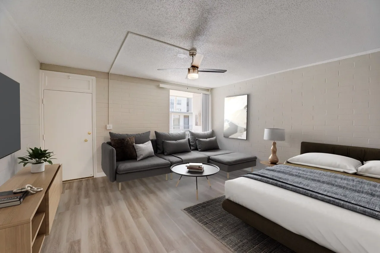 Studio with bed, gray sectional sofa, wood-style plank flooring, ceiling fan