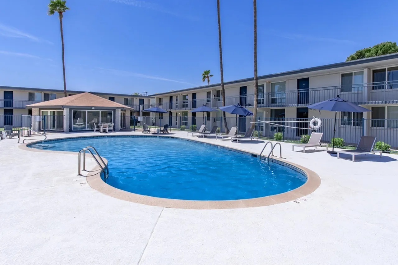 Resort-style pool, curved design, metal railings, palm trees, lounge seating, community building