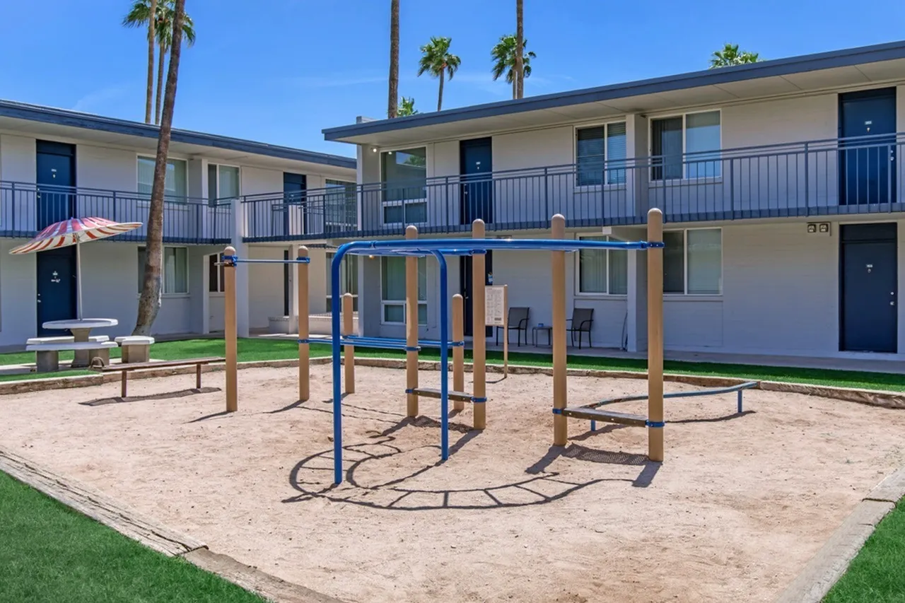 Courtyard with playground equipment, sand area, turf, palm trees, two-story residential building
