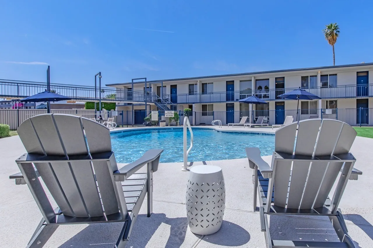 Resort-style pool, gray lounge chairs, concrete deck, multi-story apartment building