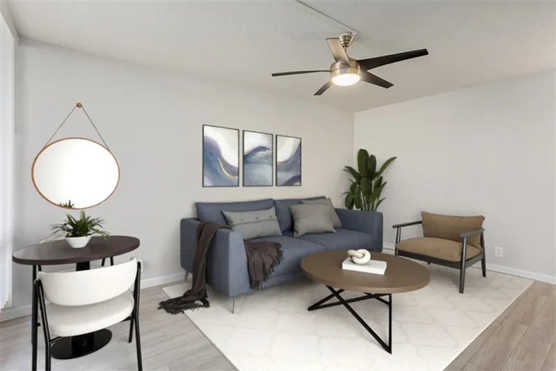 Living room with gray sofa, wood-style plank flooring, ceiling fan, round mirror, potted plant
